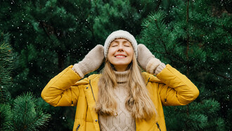 A happy young woman enjoys listening to the sounds of nature through headphones in a winter forest