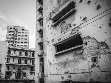 Fotografía en blanco y negro de un edificio abandonado con visibles daños e impactos de bala en sus paredes y fachada de hormigón a causas de la guerra