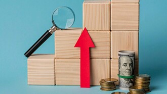 Stacks of coins and a rolled dollar bill sit beside an upward-trending block graph with a magnifying glass, symbolizing the investment and growth potential discussed in the article as crucial for achieving economic sovereignty and national strength
