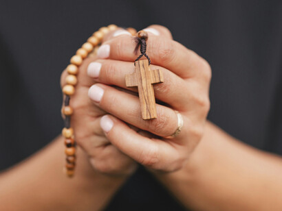 Persona rezando mientras sostiene un rosario entre las manos