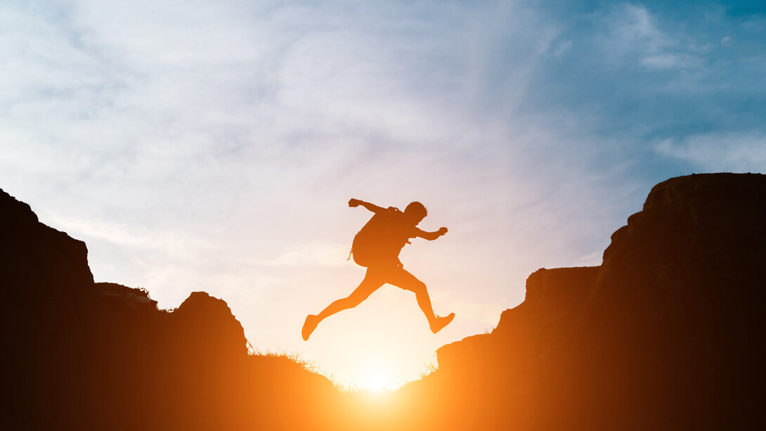 As the sun sets behind him, the man leaps across the rocks, embracing the journey, not just the destination, in his pursuit of personal growth