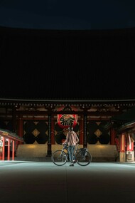 A man riding a bike in front of Sensoji Temple, Asakusa, alone under the moonlight at midnight, with the temple's iconic architecture bathed in soft, serene light, Japan
