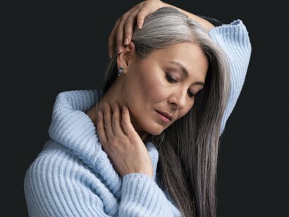 A woman gently touching her silver hair with confidence, representing how silver strands can be beautiful and meaningful