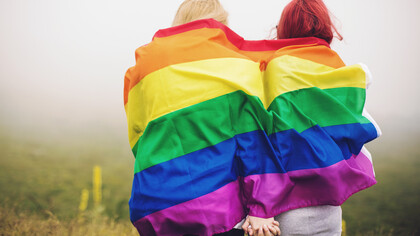 Dos mujeres se dan la mano envueltas de la bandera LGBT