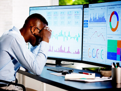An overwhelmed accountant sits before multiple computer screens, illustrating the mental strain of information overload in the digital workplace