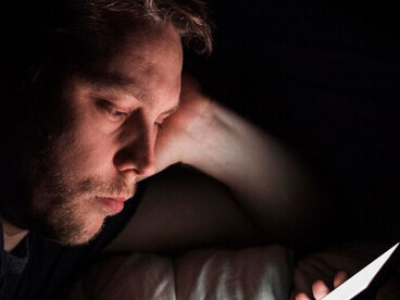 Late at night, a man stares at his phone, capturing the uneasy link between depression and digital technology