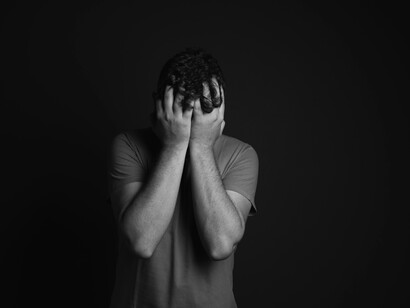 Grayscale photo of a man covering his face with his hands, depicting a moment of deep emotional strain
