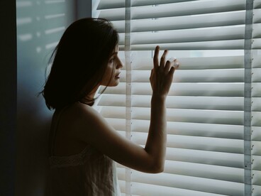 Woman gazing through hospital window as sunlight filters through the shutters