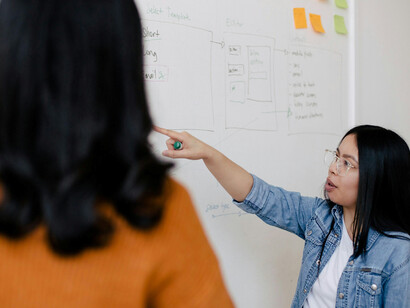 A female student in a blue tank top, standing beside a white wall, engaging with her teacher in a conversation about software engineering