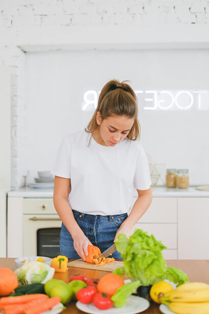 A woman slices an orange bell pepper, symbolizing a healthy, whole-food diet rich in natural vitamins and nutrients