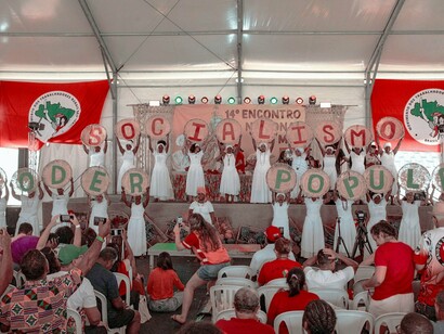 Participantes de um evento do MST exibem cartazes formando as palavras "Socialismo" e "Poder Popular". A organização coletiva é apontada no artigo como um elemento central para a reconstrução das esquerdas