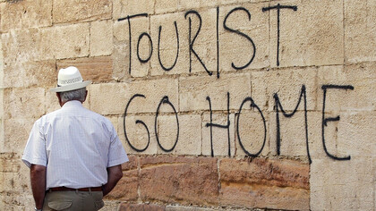 A man strolls past a wall adorned with the message "Tourists, please go home" in the Canary Islands