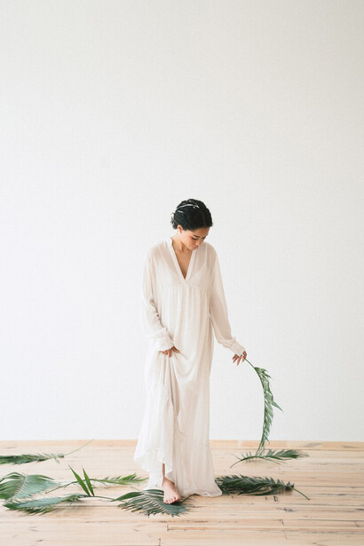 A woman in a flowing white dress sits in a quiet, empty room, representing eco-friendly, circular, and biodegradable textiles in sustainable fashion