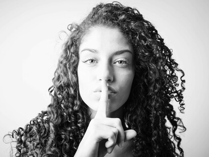 A woman with a finger against her lips is indicating a request for silence
