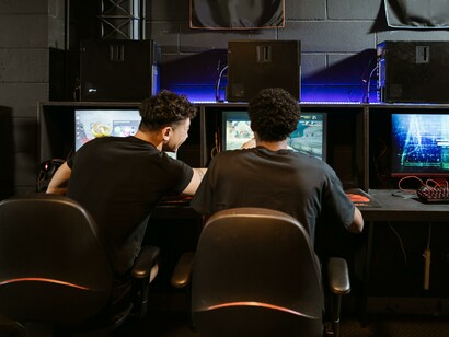 Two friends sat at computers helping each other 