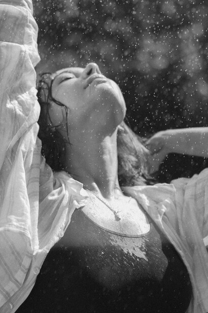 A black-and-white portrait of a joyful woman laughing as she stands in the rain