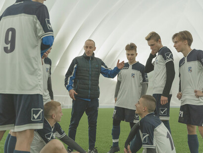 A coach giving instructions to his team, alongside a director of football and a football manager in discussion
