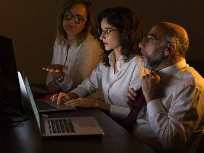 Colleagues discussing work in a dimly lit office while working on computers
