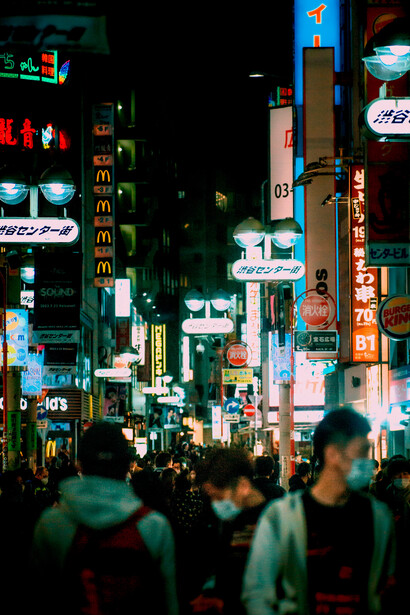 Crowds walking through a brightly lit street of buildings and neon signs at night in Tokyo, Japan
