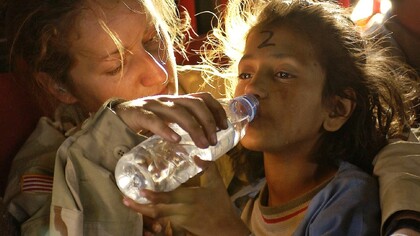 Soldier gives a drink of water to a child refugee
