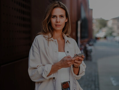 A woman in a white coat, actively engaged as a social media manager, confidently handles her phone