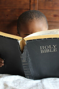Boy reading Holy Bible while lying on bed