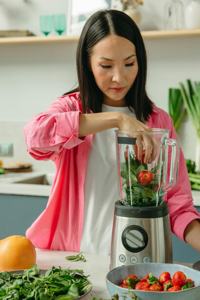 A woman drinking a smoothie alongside a balanced plate of healthy foods, featuring fresh fruits and vegetables