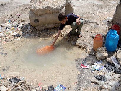 Un niño recoge agua al costado de una carretera en Alepo