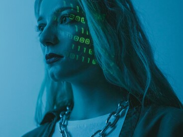 O rosto de uma mulher é iluminado por códigos projetados digitalmente. Estudos apontam que modelos de linguagem ainda associam homens e mulheres a papéis sociais distintos. A inteligência artificial aprende a partir de informações produzidas por sociedades marcadas por desigualdades. Especialistas defendem auditorias e testes mais rigorosos para identificar preconceitos em sistemas de IA
