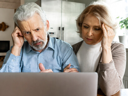 An upset senior couple reacts to alarming information on their laptop, reflecting the emotional impact of internet fraud