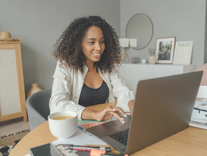 A woman in a white blazer using a MacBook Pro at a brown wooden table