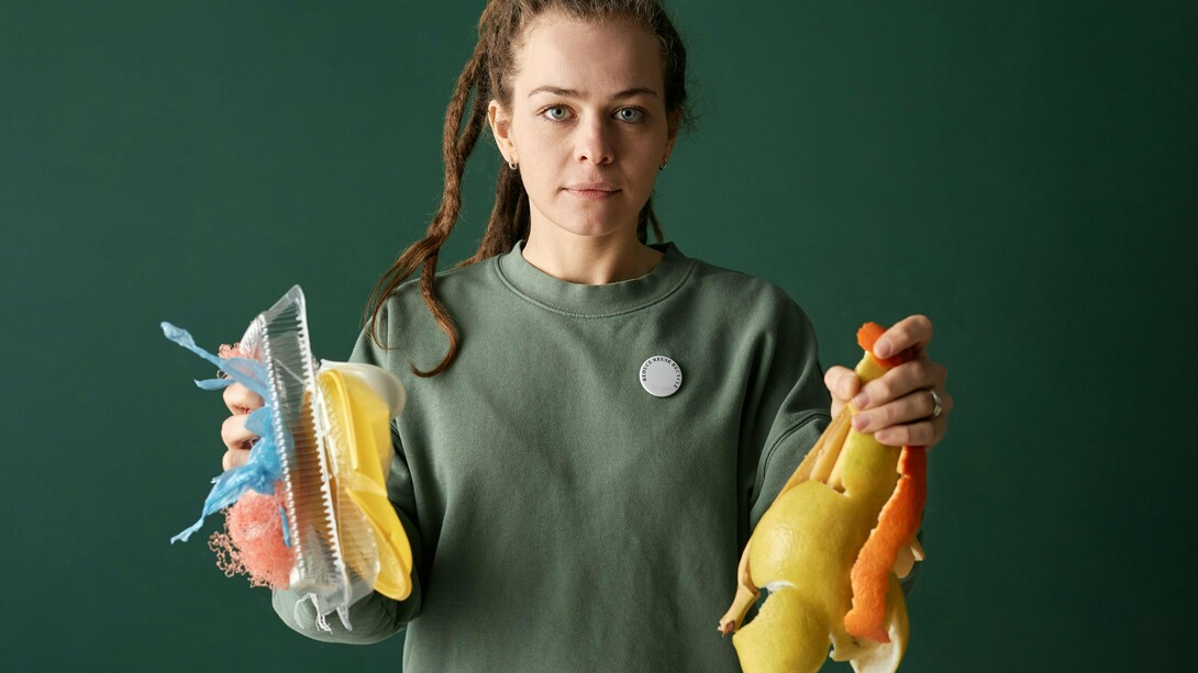 Uma mulher segura resíduos plásticos em uma mão e resíduos orgânicos na outra, evidenciando dois destinos possíveis para os materiais descartados. Entre o passivo ambiental e a matéria-prima do futuro, a escolha define o modelo de desenvolvimento. A imagem simboliza o contraste entre a linearidade do descarte e o potencial regenerativo da biomassa. A transição para uma economia circular começa na forma como enxergamos o lixo