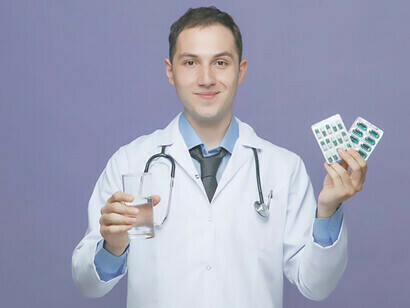 Jovem médico do sexo masculino segurando medicamentos felizmente, vestido em jaleco médico com estetoscópio ao redor do pescoço