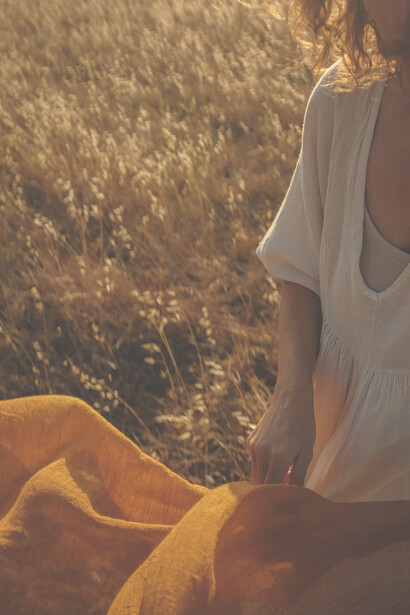 A woman sits gracefully in a field, adorned in a flowing white dress that harmonizes with the natural surroundings, creating a serene and picturesque scene