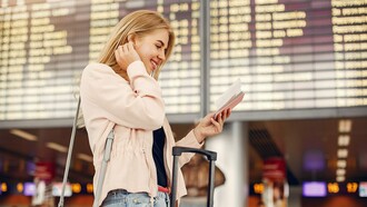 A smiling traveler checks her passport in front of an airport departures board, reflecting the article’s focus on mindful preparation and a stress-free travel mindset
