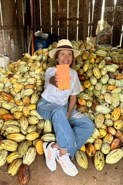 Silvia Guédez sobre una pila de granos de cacao, mostrando una de las barras de su marca