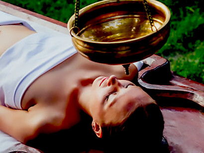 A serene Shirodhara oil therapy session, an ancient Ayurvedic healing practice, with a woman lying peacefully on a wooden table in a traditional Indian wellness salon