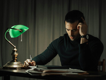 An elegant man reading a book at a table with a retro lamp