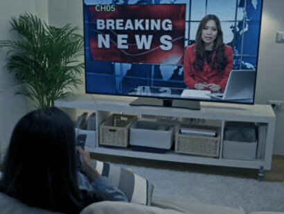 A woman relaxes on her couch, glued to the TV, as the nonstop political news broadcast intensifies her sense of stress and overwhelm