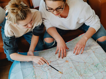A woman and her daughter planning a trip together, pointing at a map in a mindful travel moment