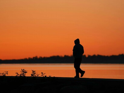 Pessoa caminhando segue seu caminho em meio à luz suave do entardecer refletida na água. Nem sempre é preciso resolver cada pensamento; às vezes, basta continuar a caminhar