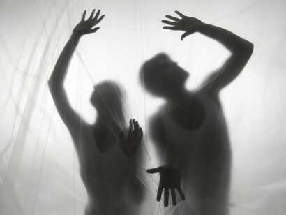 Two people concealed behind a curtain-like veil, reflecting the eerie pull of the supernatural