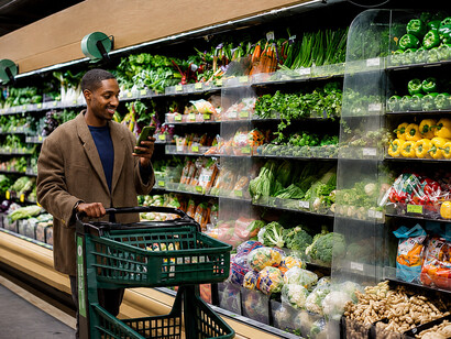 Customer selecting fresh fruits and vegetables in a supermarket aisle, highlighting modern shopping habits and food choices