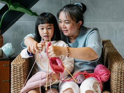 A lesson in knitting between a grandparent and granddaughter, reflecting how culture survives through patient guidance and shared practice