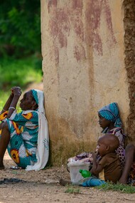 An elderly woman and children sitting on the ground, illustrating the everyday realities of poverty and malnutrition
