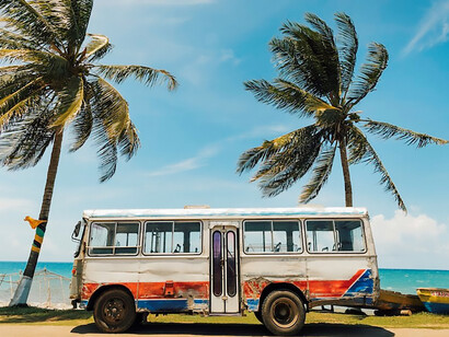 Beneath the radiant Jamaican sky, a white and blue bus stands gracefully by a swaying palm tree, creating a picturesque scene 