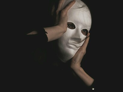 A person holding on tightly to the mask, showing how power is often used from behind veils of secrecy
