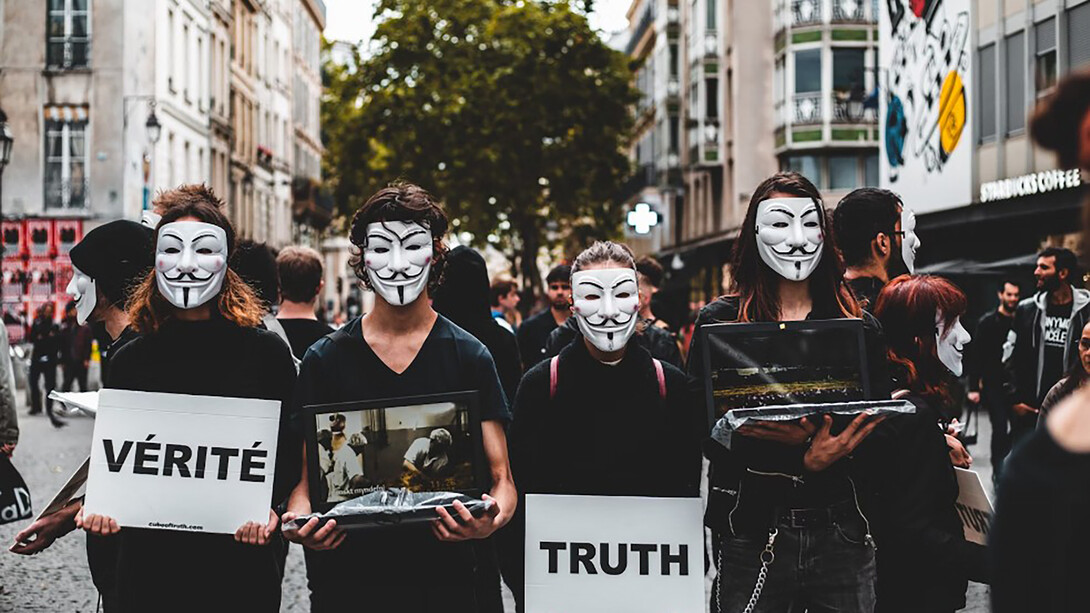 Four people wearing Guy Fawkes masks protest against disinformation, boldly demanding truth and transparency