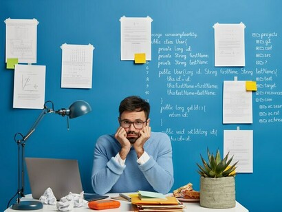 A frustrated male programmer in glasses sits at his workstation, embodying the mental toll of long hours and unresolved code errors