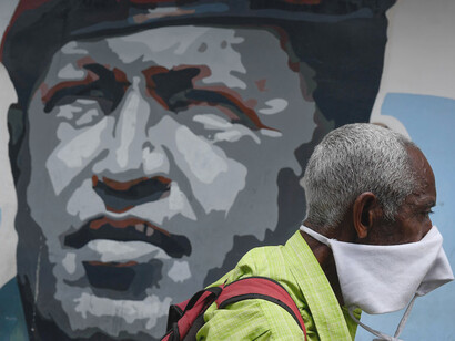 Ciudadano venezolano trata de sortear la pandemia en Caracas, de fondo un mural de Hugo Chávez